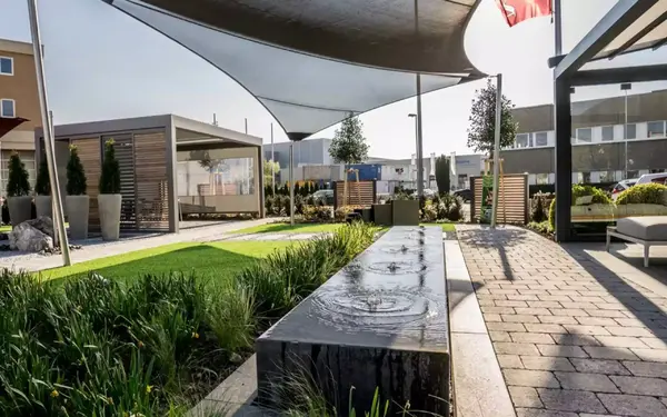 Moderner Garten mit Wasserbecken, Sonnensegel, Pavillon und gepflegtem Rasen.