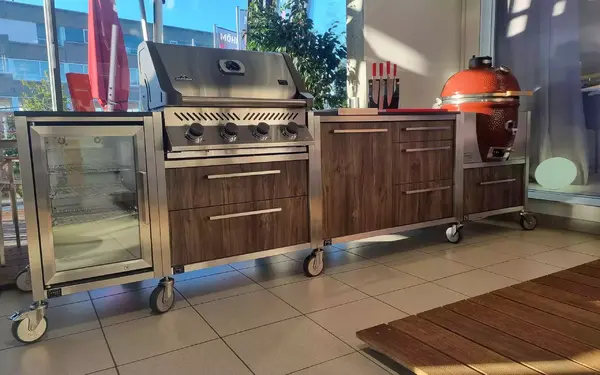 Moderne Outdoor-Küche mit Grill, Kühlschrank, Holzfronten und Keramikgrill auf Rollen.