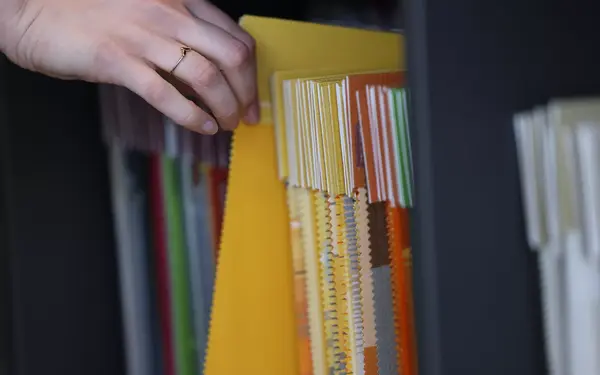 Eine Hand blättert durch bunte Stoffmuster für Innenausstattung und Textildesign.