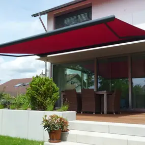 Moderne Terrassenüberdachung mit roter Markise an einem Einfamilienhaus im Garten.