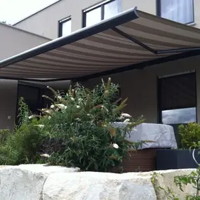 Moderne Terrasse mit Markise und Garten, idealer Sonnenschutz am Haus für den Außenbereich.