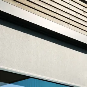 Moderner textiler Sonnenschutz als Außenrollo an einer Holzfassade mit Fenster.