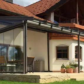 Moderner Wintergarten mit Glasüberdachung an Einfamilienhaus im Grünen bei Sonnenschein.