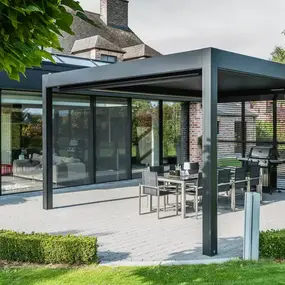 Moderne Terrassenüberdachung aus Aluminium mit Sitzgruppe und Grill im gepflegten Garten.