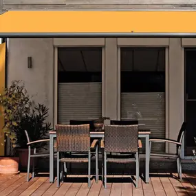 Terrasse mit gelber Markise, Sichtschutz, Holzboden und Gartenmöbeln vor Hausfassade.