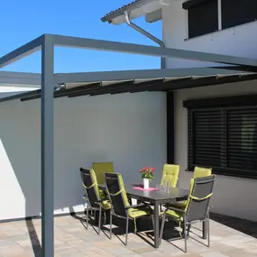 Moderne Terrassenüberdachung aus Aluminium am Haus mit Sitzgruppe und Gartenblick.